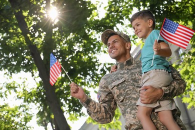 Photo of Soldier and his little son with American flags outdoors, low angle view. Veterans Day in USA