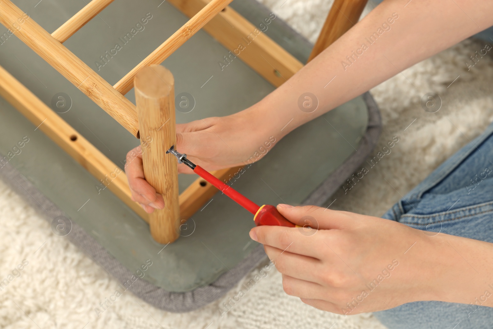 Photo of Woman with screwdriver assembling furniture on carpet, closeup