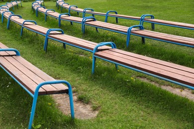 Modern wooden benches on green grass in park
