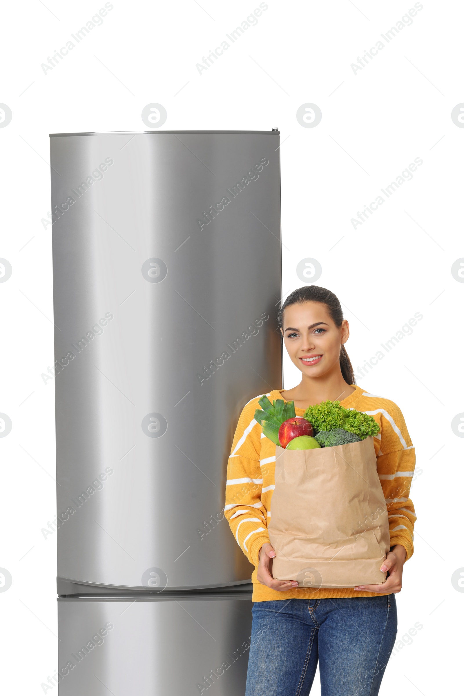 Photo of Young woman with bag of groceries near closed refrigerator on white background