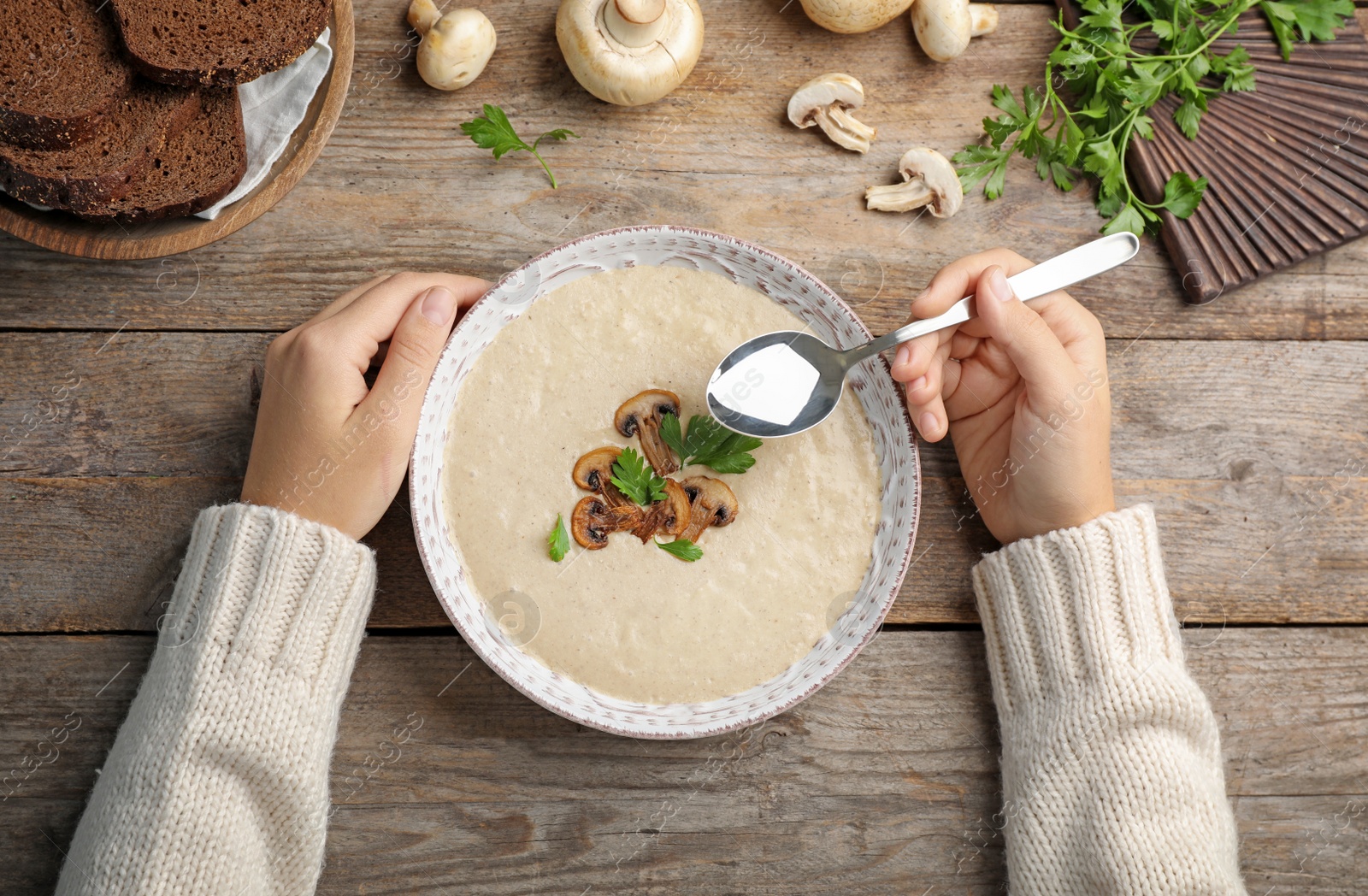 Photo of Woman eating fresh homemade mushroom soup from bowl on table, top view