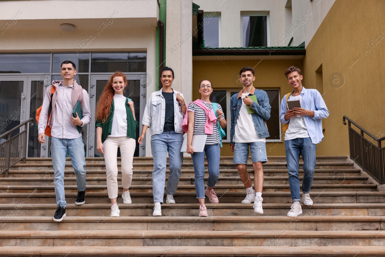 Photo of Group of happy young students walking down stairs outdoors