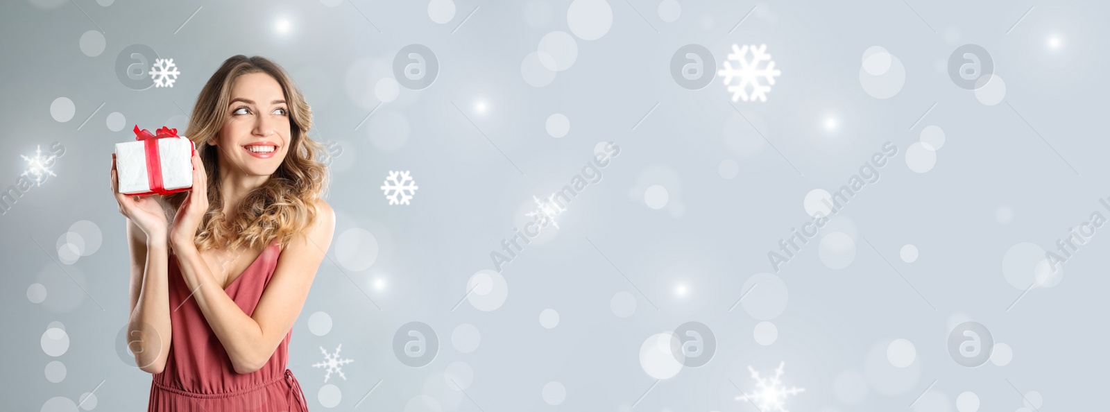 Image of Beautiful woman holding Christmas gift box on light grey background, space for text. Banner design