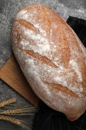Photo of Loaf of tasty sodawater bread and wheat spikes on grey table, flat lay