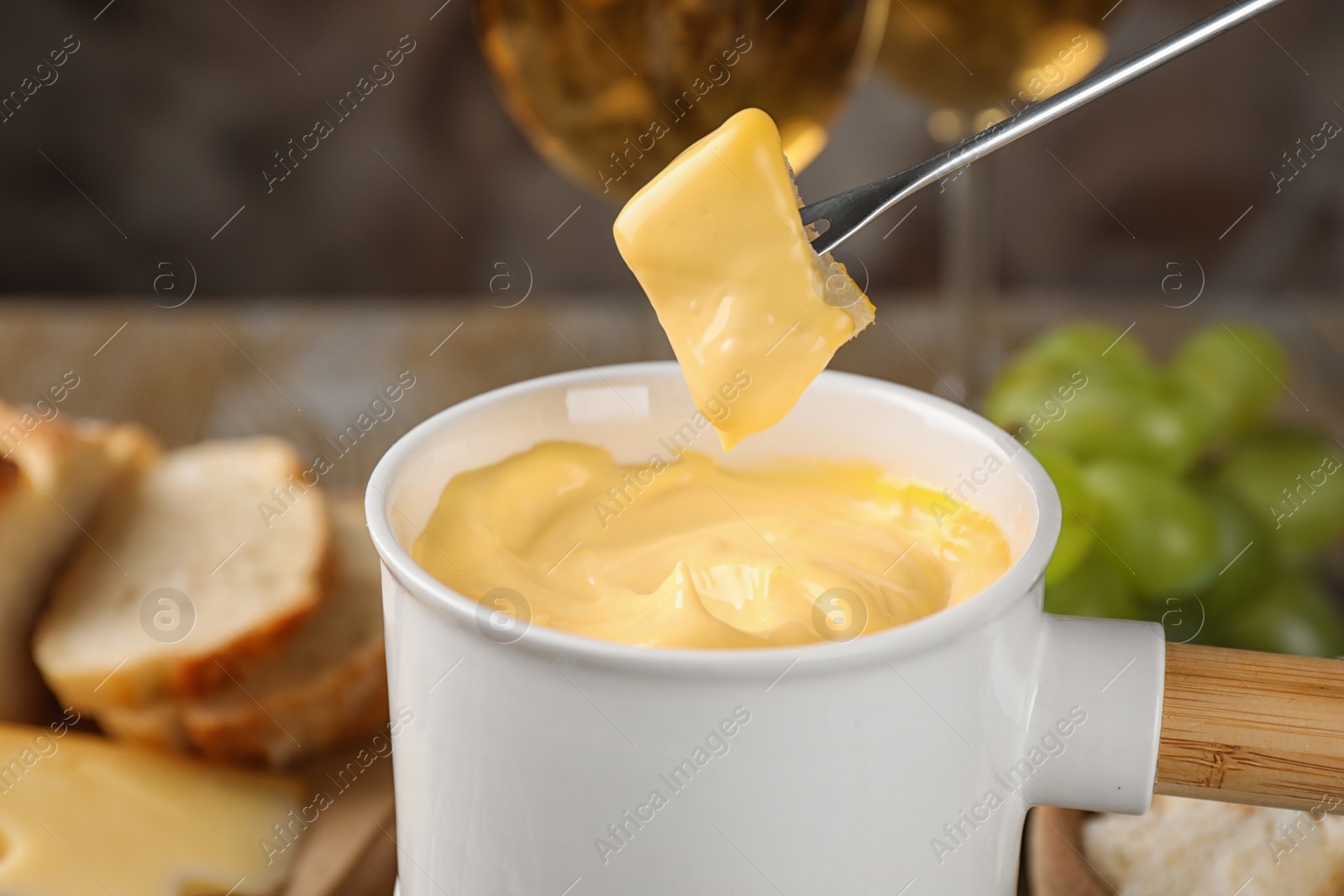 Photo of Dipping piece of cheese into tasty cheese fondue on table, closeup view