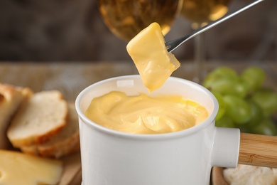 Photo of Dipping piece of cheese into tasty cheese fondue on table, closeup view