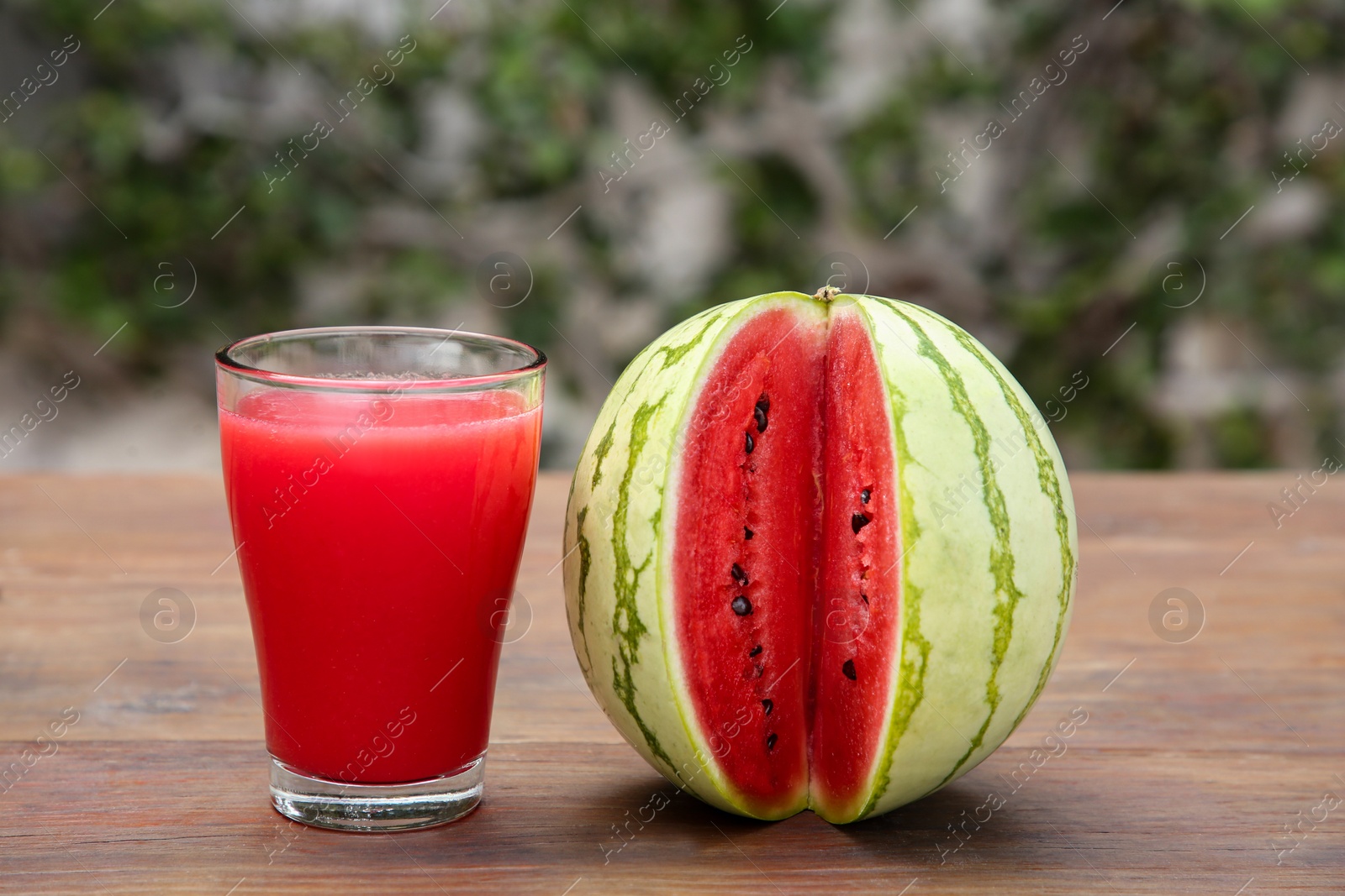 Photo of Delicious ripe watermelon and glass of fresh juice on wooden table outdoors