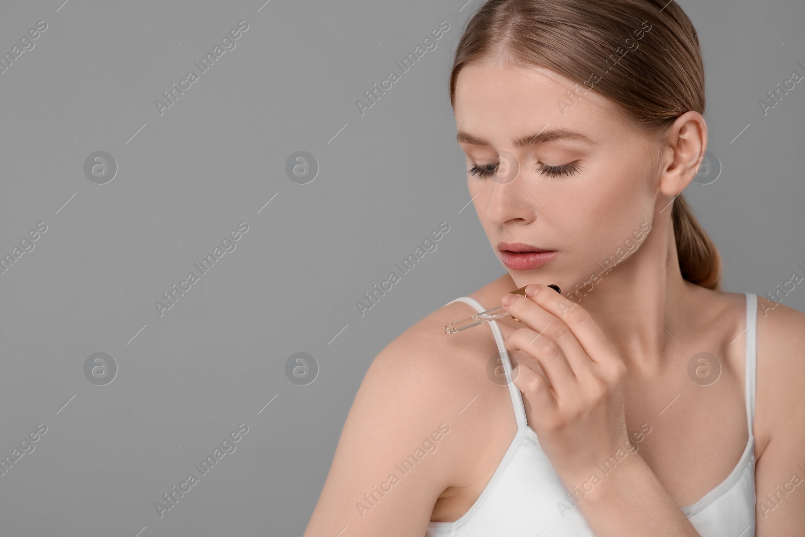 Photo of Beautiful young woman applying essential oil onto shoulder on grey background. Space for text