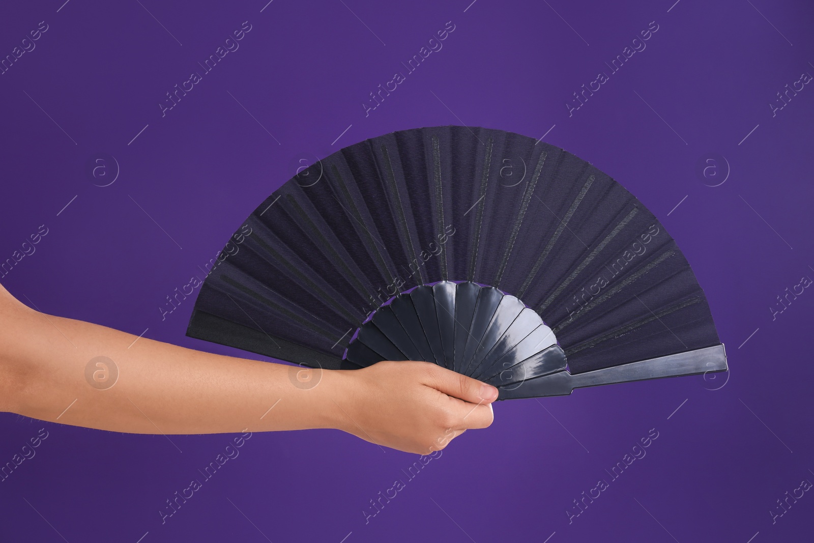 Photo of Woman holding black hand fan on purple background, closeup