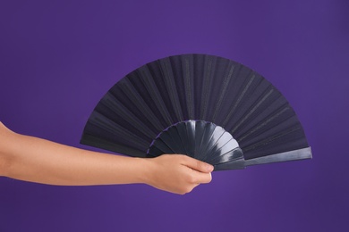 Photo of Woman holding black hand fan on purple background, closeup