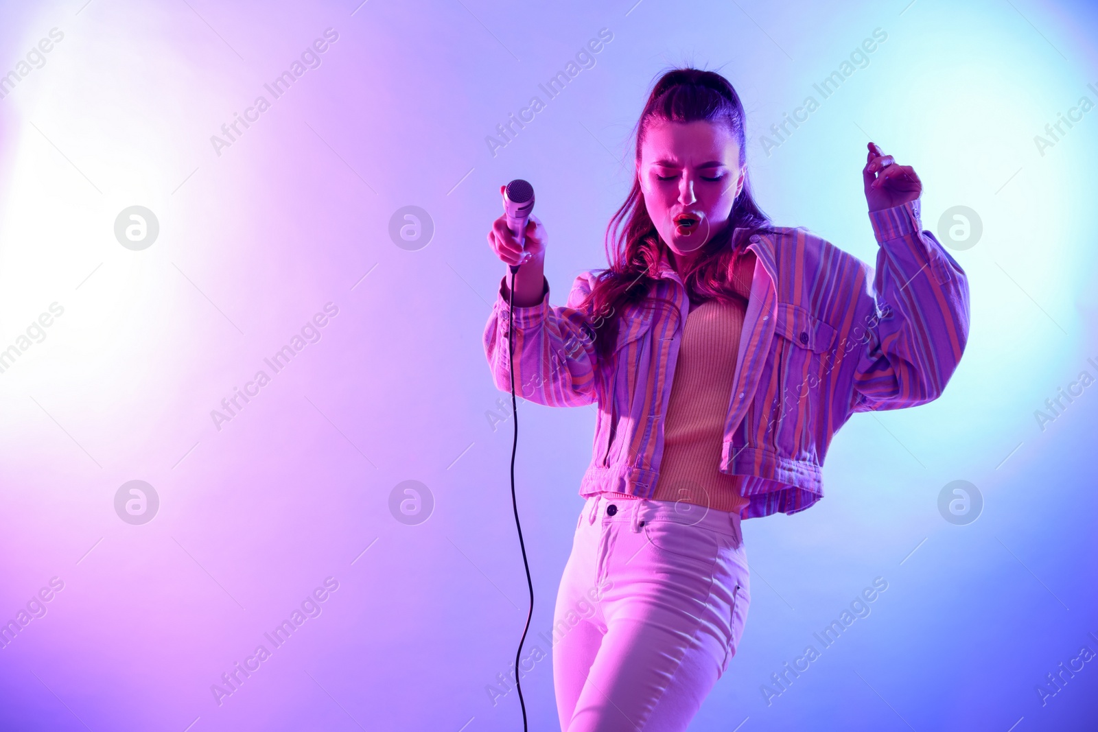 Photo of Beautiful singer with microphone performing on bright background. Space for text