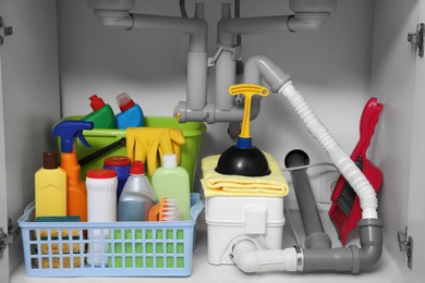 Photo of Open under sink cabinet with different cleaning supplies in kitchen