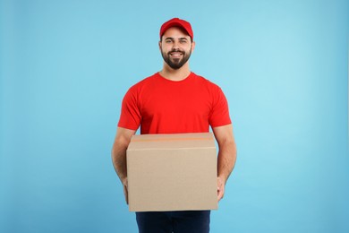 Happy young courier with parcel on light blue background