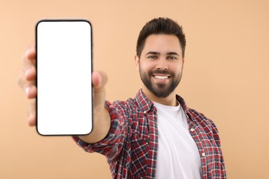 Photo of Young man showing smartphone in hand on beige background