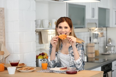 Photo of Beautiful woman eating tasty toasted bread with jam at table