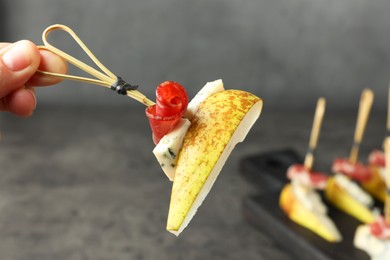 Woman holding tasty canape with pear, blue cheese and prosciutto at table, closeup