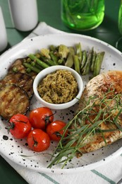 Photo of Tasty chicken, vegetables with tarragon and pesto sauce served on table, closeup
