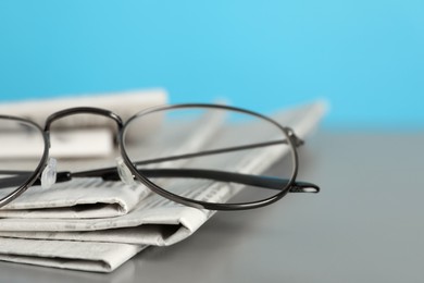 Stack of newspapers and glasses on grey table against light blue background, closeup