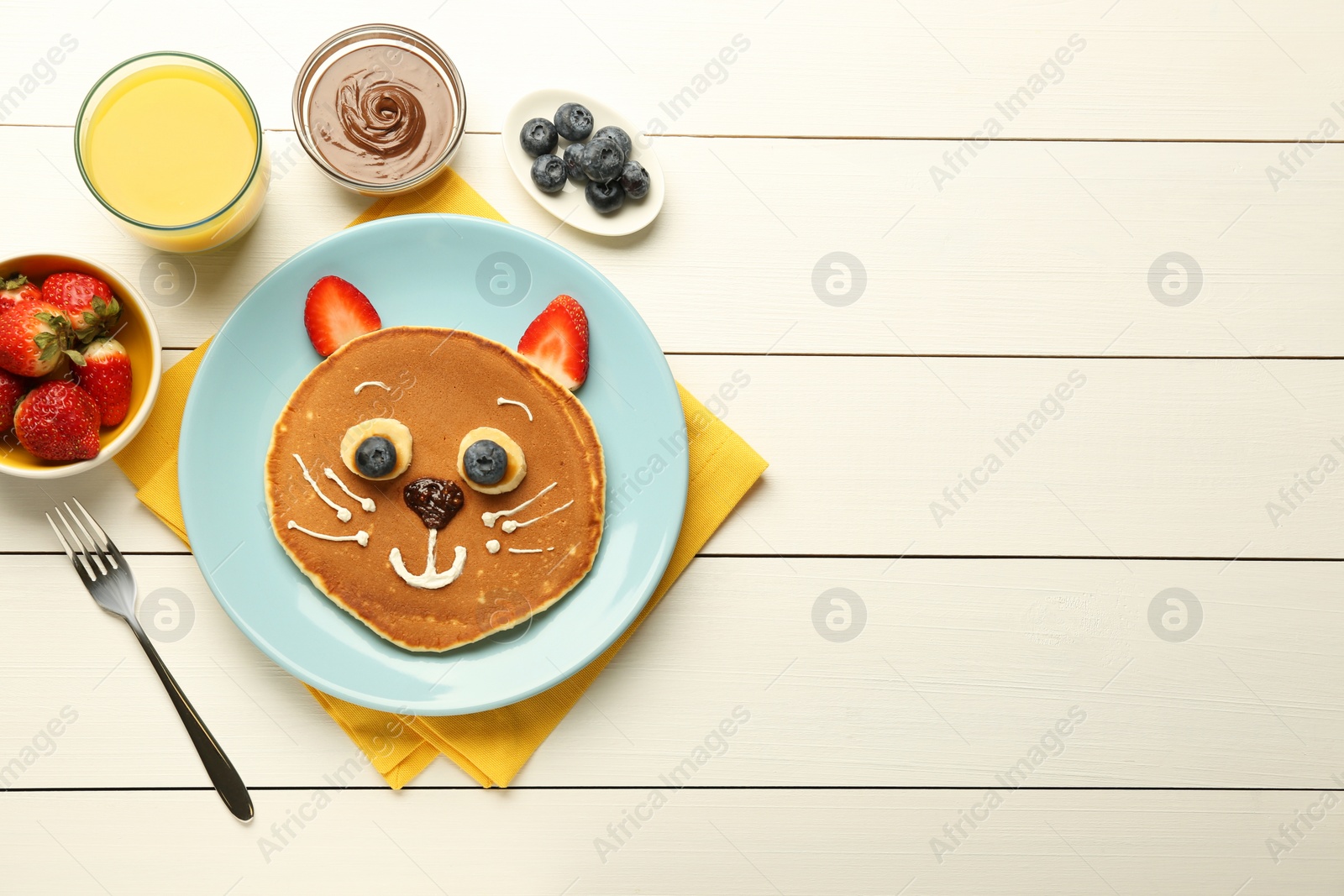 Photo of Creative serving for kids. Plate with cute cat made of pancakes, berries, cream, banana and chocolate paste on white wooden table, flat lay. Space for text