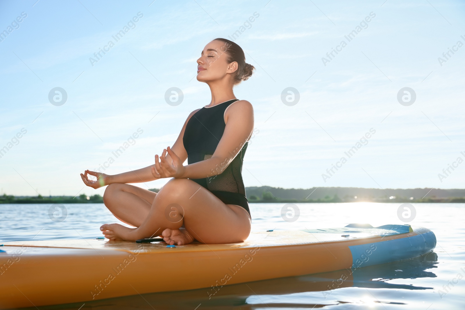 Photo of Young meditating yoga on color SUP board on river at sunset