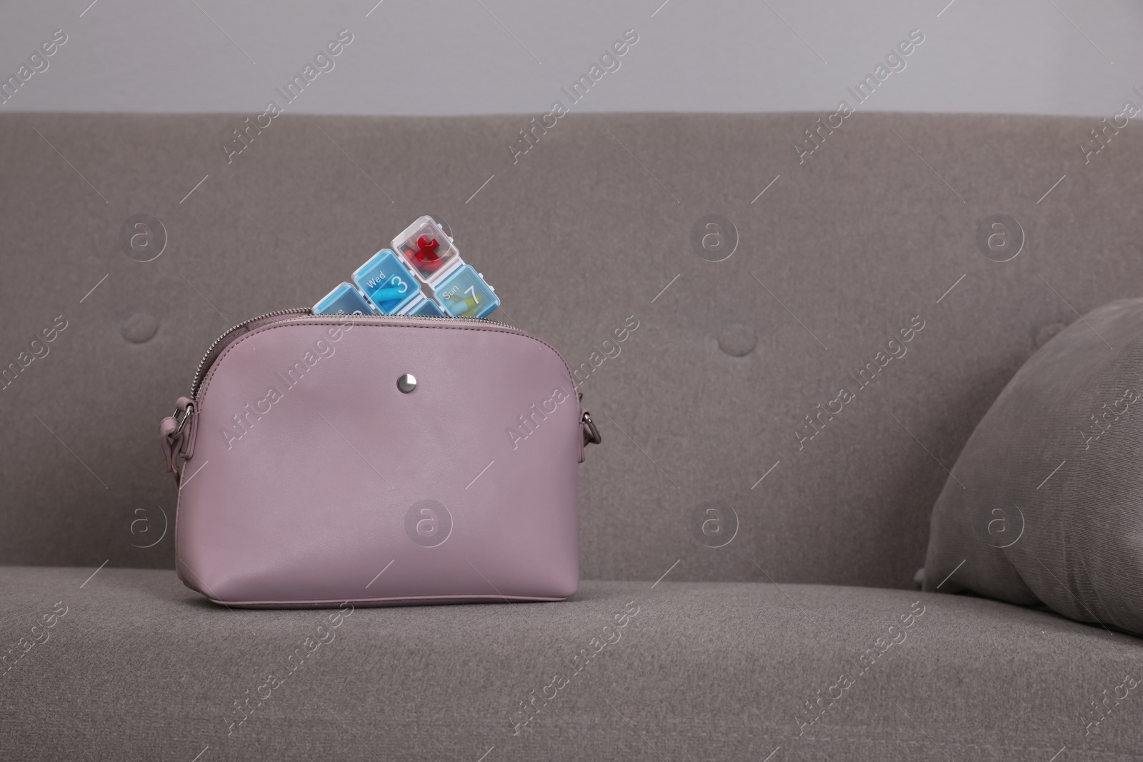 Photo of Stylish women's bag with plastic pill box on sofa indoors. Space for text