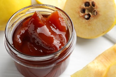 Photo of Tasty homemade quince jam in jar and fruits on white table, closeup