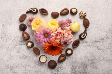 Photo of Heart made with delicious chocolate candies and beautiful flowers on grey table, flat lay