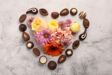 Heart made with delicious chocolate candies and beautiful flowers on grey table, flat lay