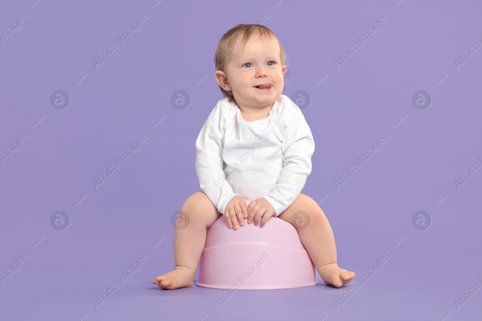 Photo of Little child sitting on baby potty against violet background