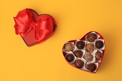 Photo of Heart shaped box with delicious chocolate candies on yellow background, flat lay