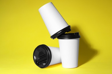 Photo of Paper cups with black lids on yellow background. Coffee to go