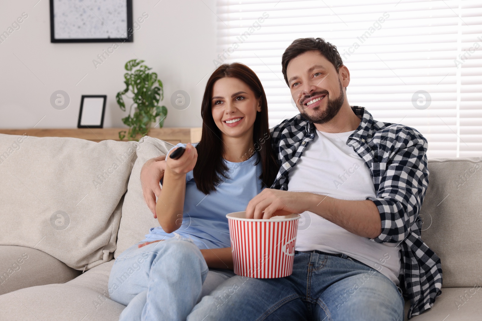 Photo of Happy couple watching show at home. Woman changing TV channels with remote control