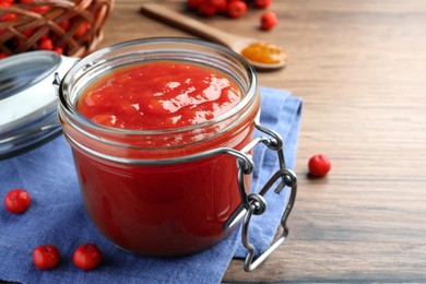 Photo of Delicious rowan jam in glass jar on wooden table. Space for text