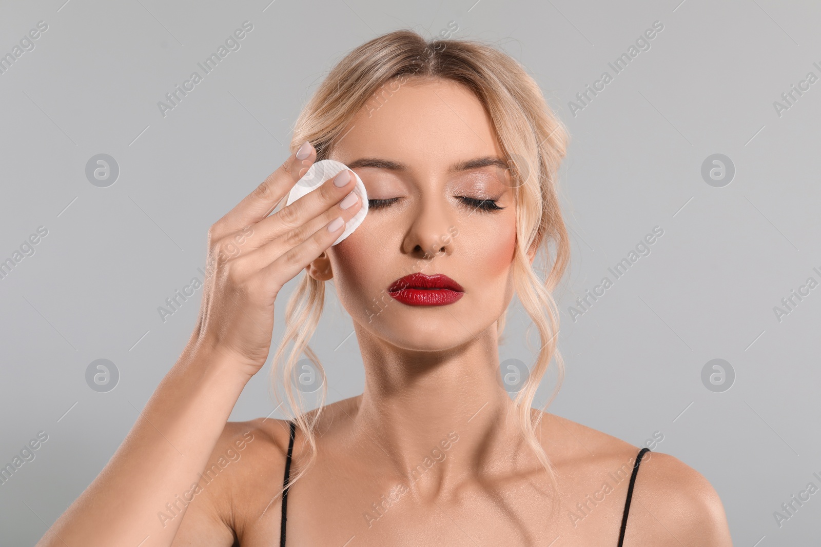 Photo of Beautiful woman removing makeup with cotton pad on light grey background
