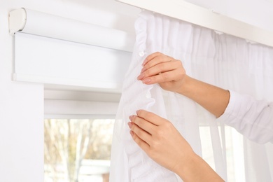 Woman hanging window curtain indoors, closeup. Interior decor element