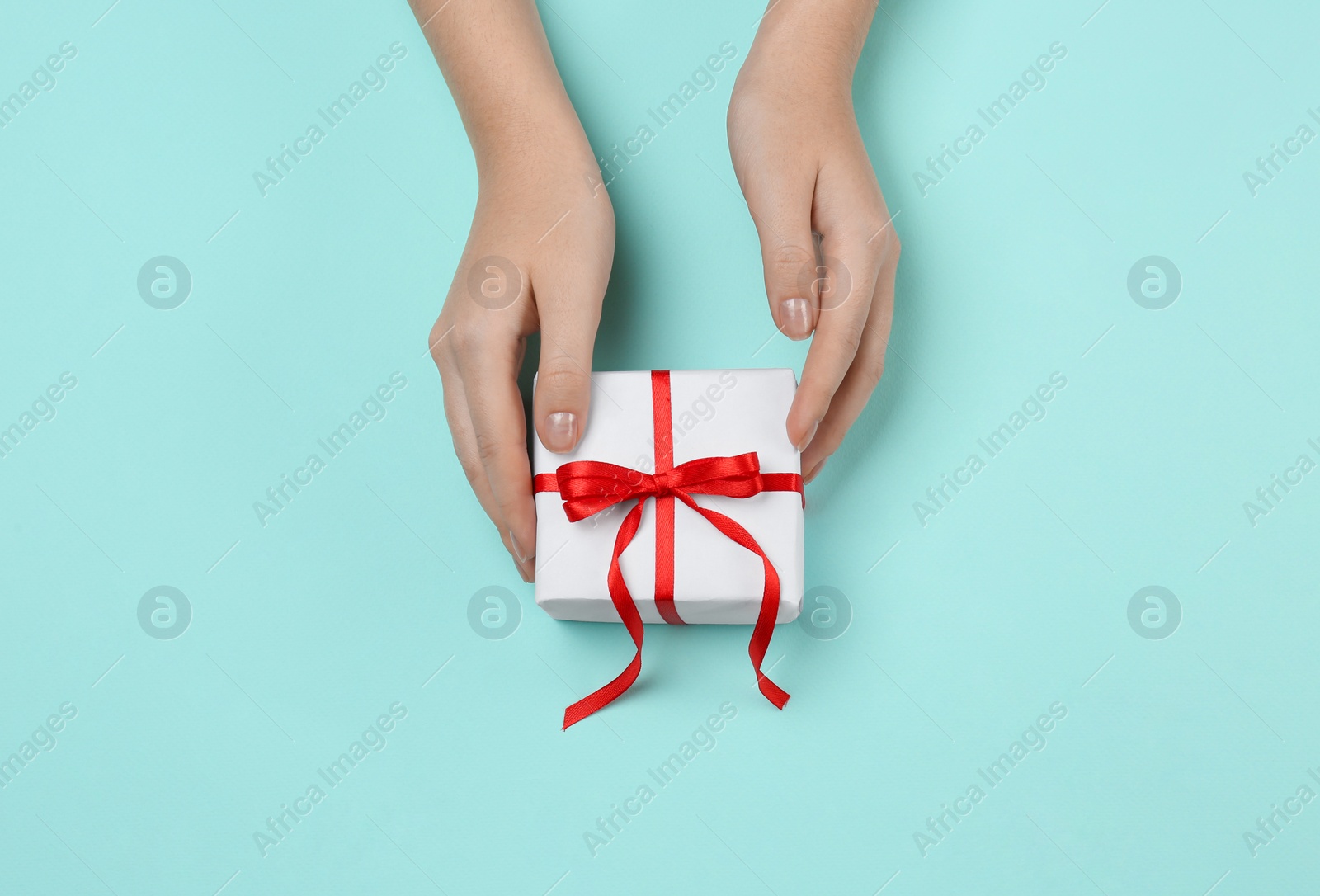 Photo of Woman holding beautiful gift box on turquoise background, top view