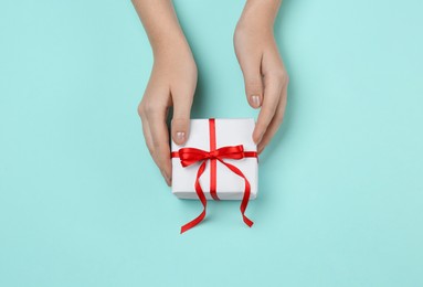 Woman holding beautiful gift box on turquoise background, top view