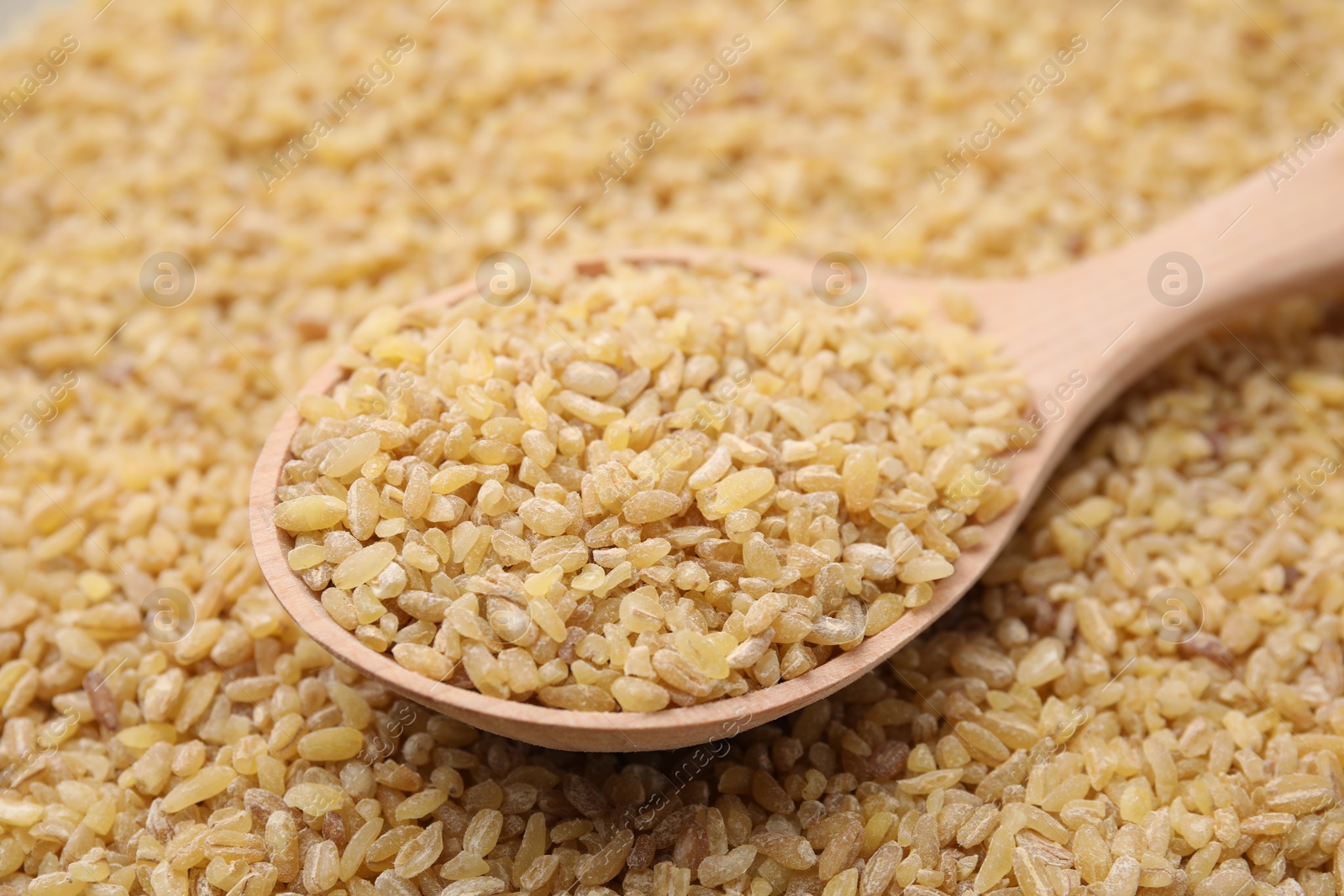 Photo of Wooden spoon and uncooked organic bulgur as background, closeup