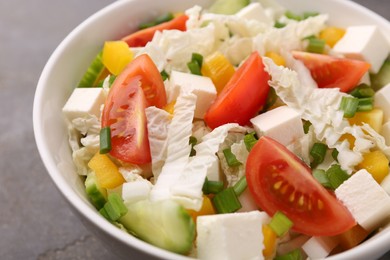 Photo of Tasty salad with Chinese cabbage, tomato, cheese, pepper and cucumber on grey table, closeup