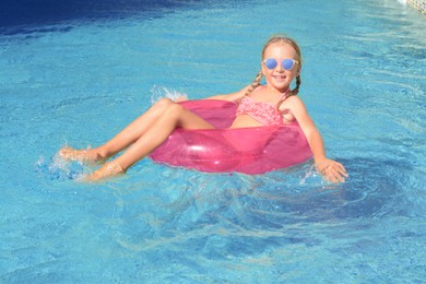 Photo of Cute little girl with inflatable ring in pool on sunny day