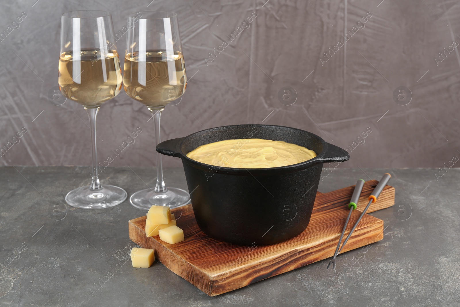 Photo of Fondue pot with tasty melted cheese, forks and wine on grey table