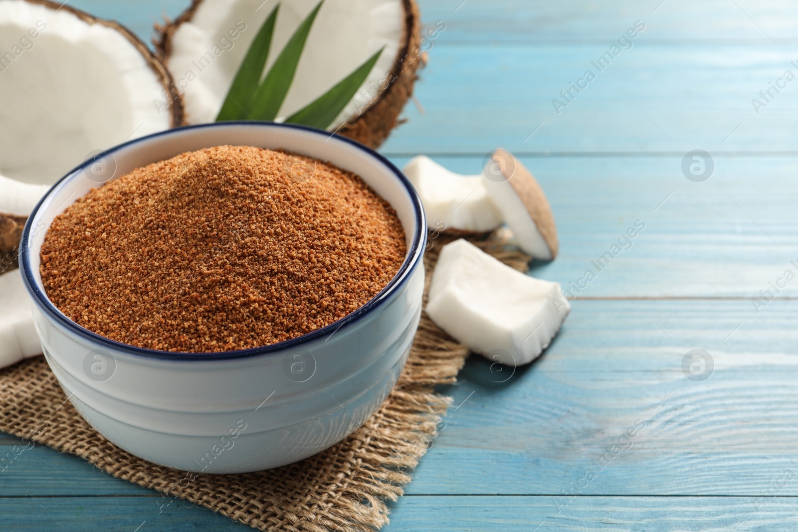 Photo of Natural coconut sugar in bowl on light blue wooden table, space for text