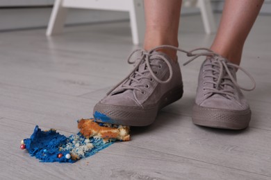 Photo of Woman stepping on dropped cupcake indoors, closeup. Troubles happen