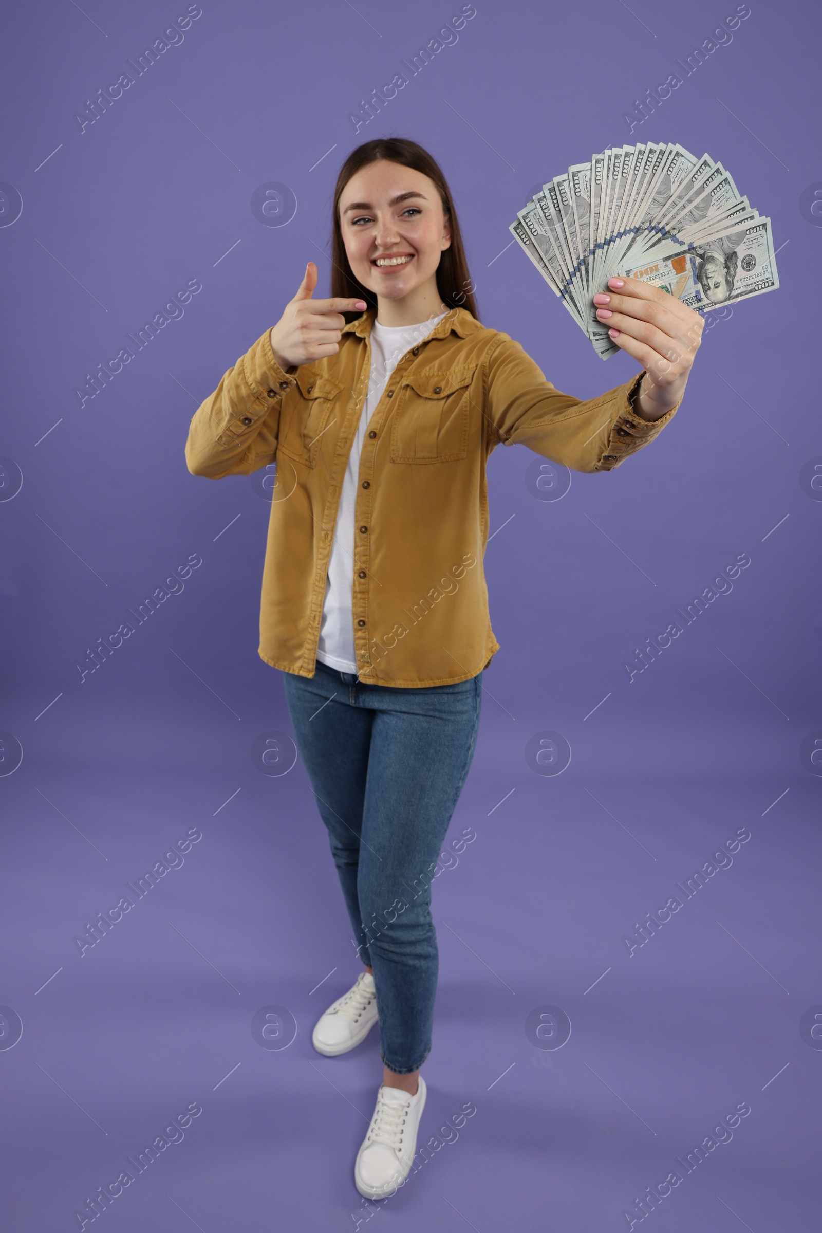 Photo of Happy woman pointing at dollar banknotes on purple background