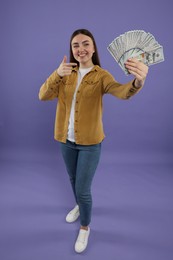 Happy woman pointing at dollar banknotes on purple background