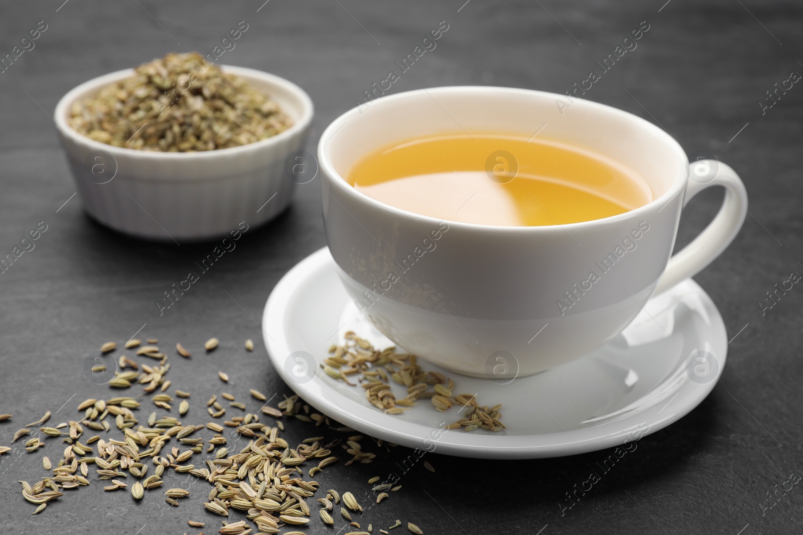 Photo of Aromatic fennel tea in cup and seeds on black table, closeup. Space for text