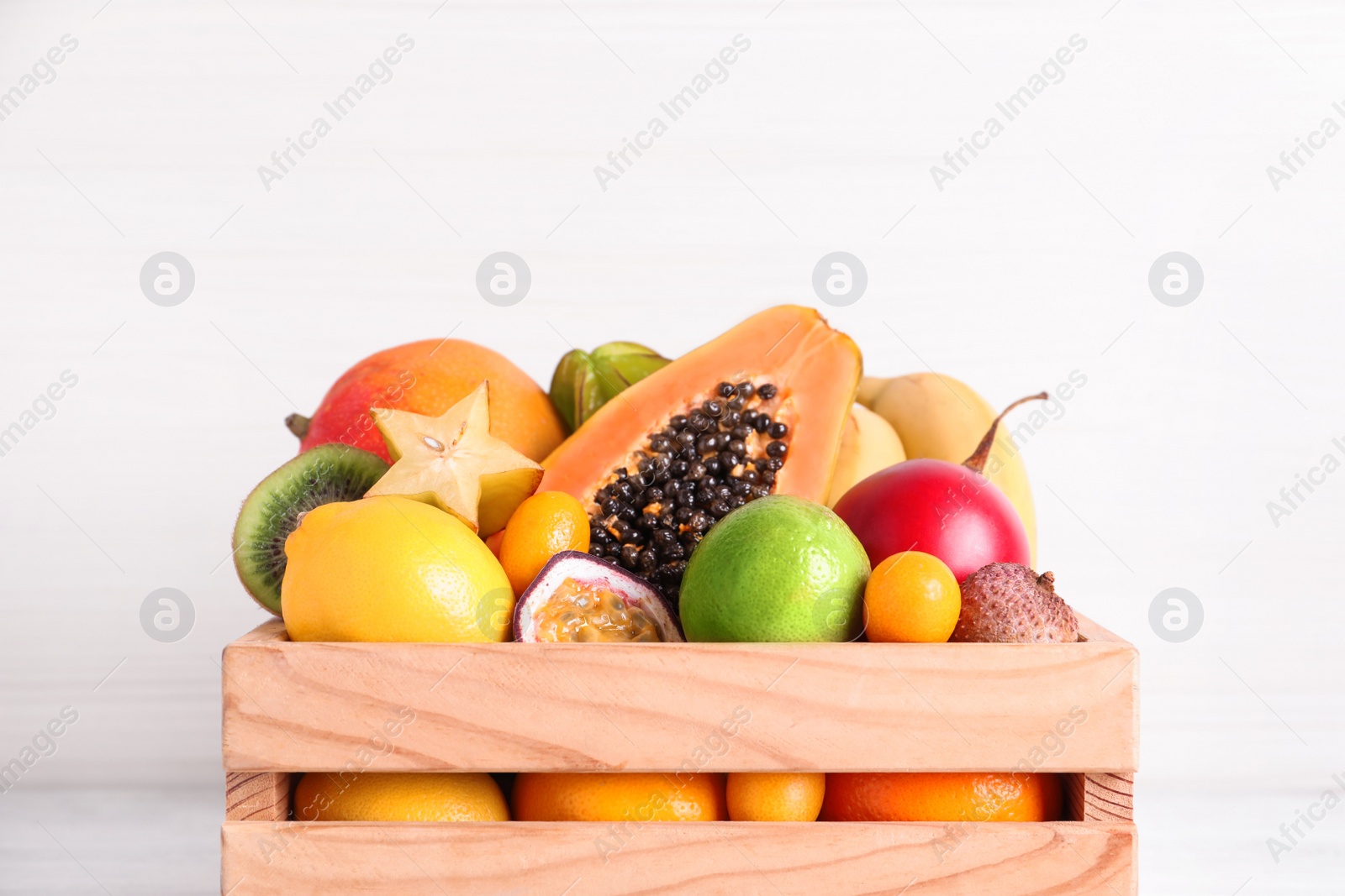 Photo of Different tropical fruits in wooden box on white background, closeup