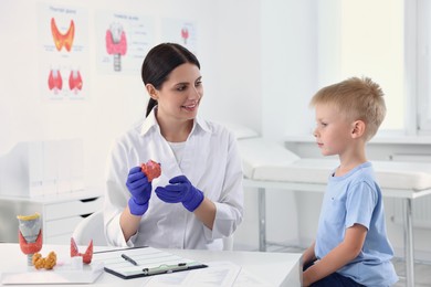 Photo of Endocrinologist showing thyroid gland model to little patient at table in hospital