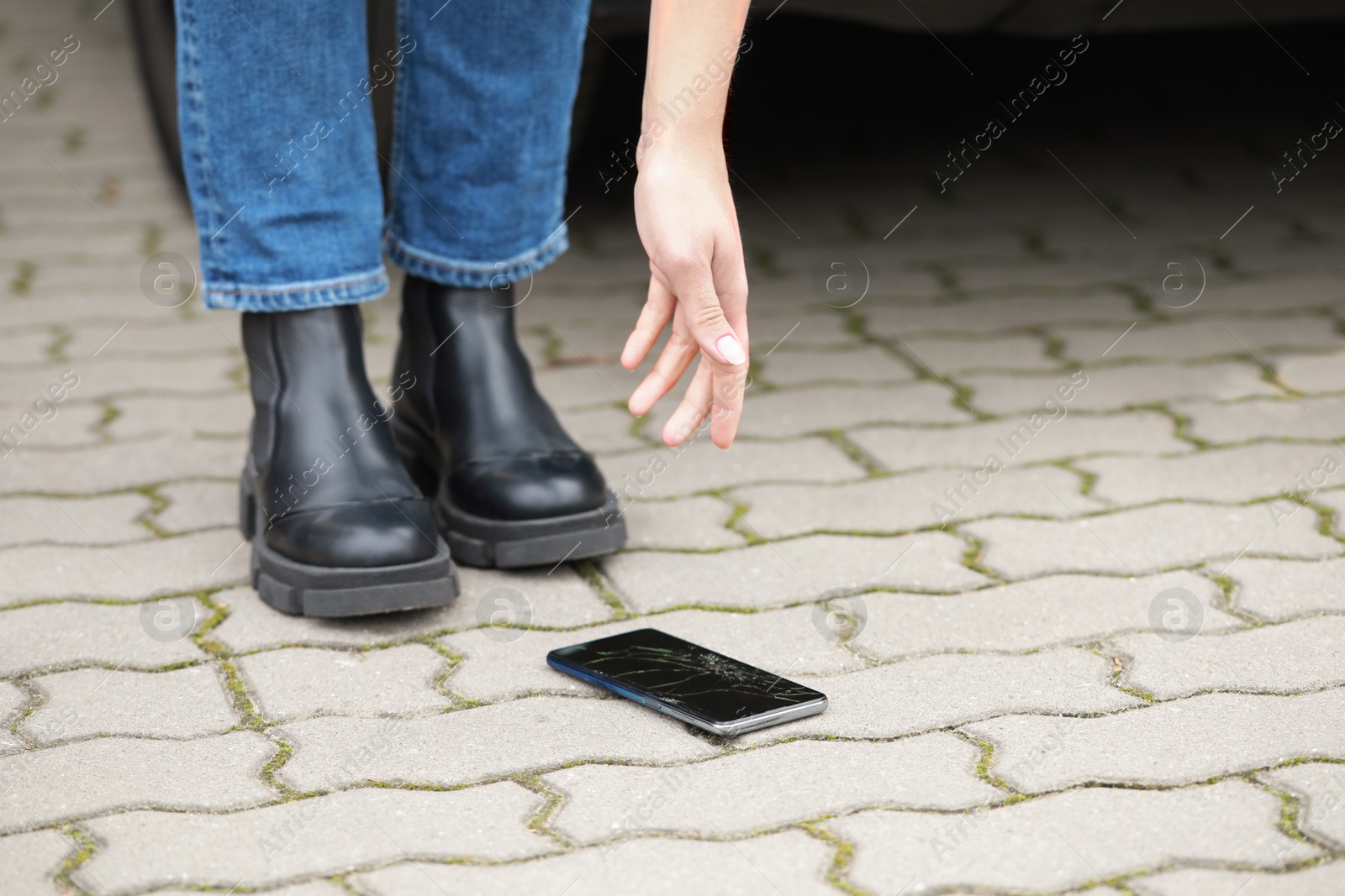 Photo of Woman taking dropped smartphone from pavement, closeup. Device repairing