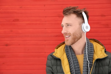 Photo of Young man listening to music with headphones against color wall. Space for text